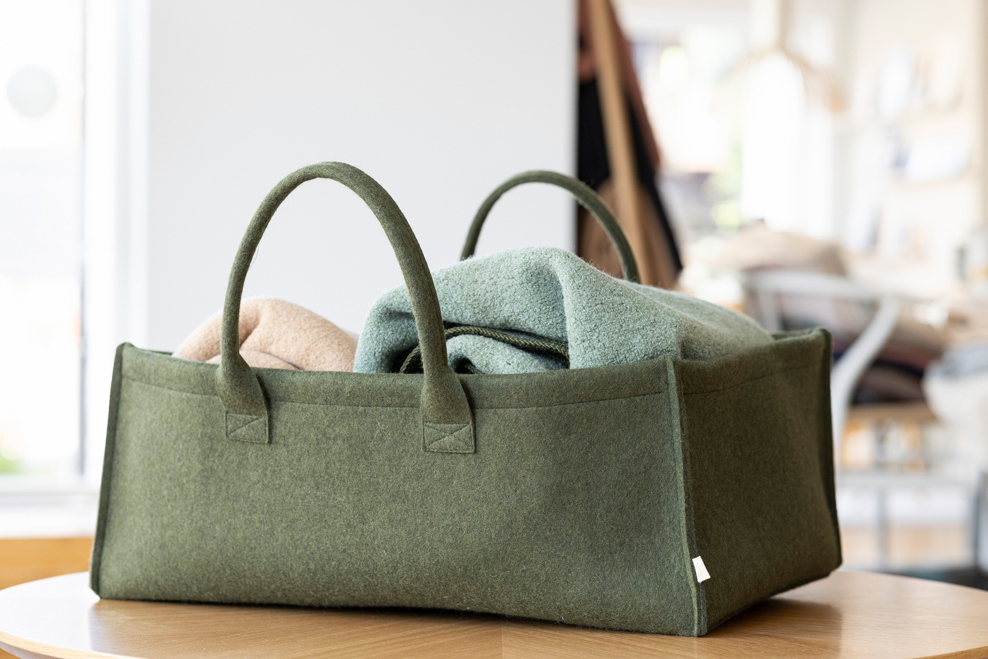 Großer disana Filz Aufbewahrungs-Korb in Oliv mit Tragegriffen, gefüllt mit Decken aus Bio-Merinowolle auf einem Holztisch.