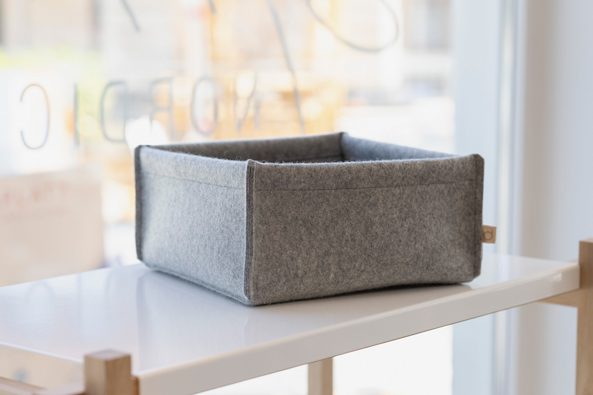 Kleine graue disana Filz-Box aus Bio-Recycling-Filz auf einem weißen Regal vor einem hellen Fensterhintergrund.