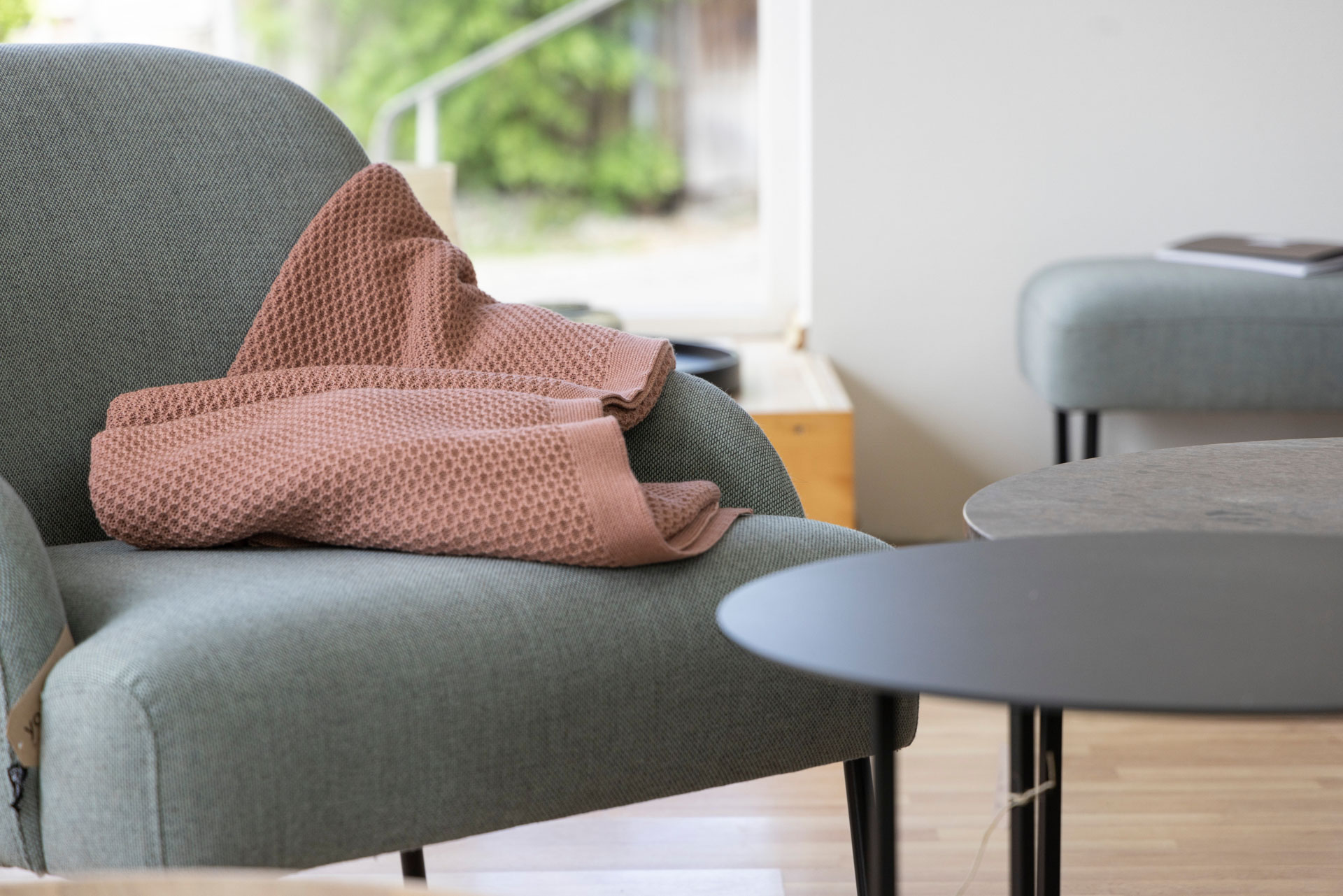 disana Waben-Strickdecke, Rosé auf einem hellgrauen Sessel drapiert in einem hellen Wohnzimmer mit Holzparkett & Tischchen