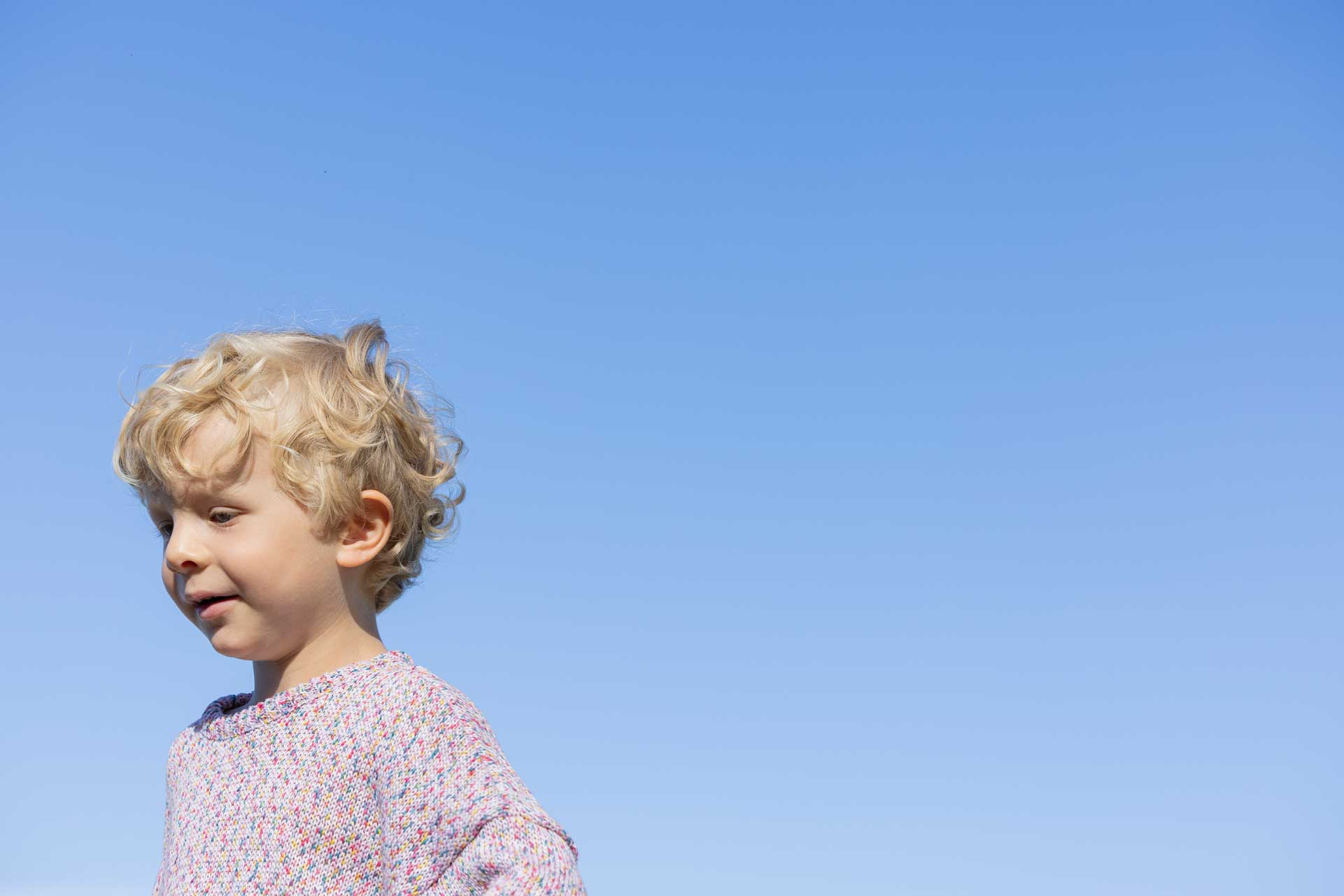 A child wears the disana Cotton Jumper "Spray" in soft pink, against a backdrop of bright blue sky
