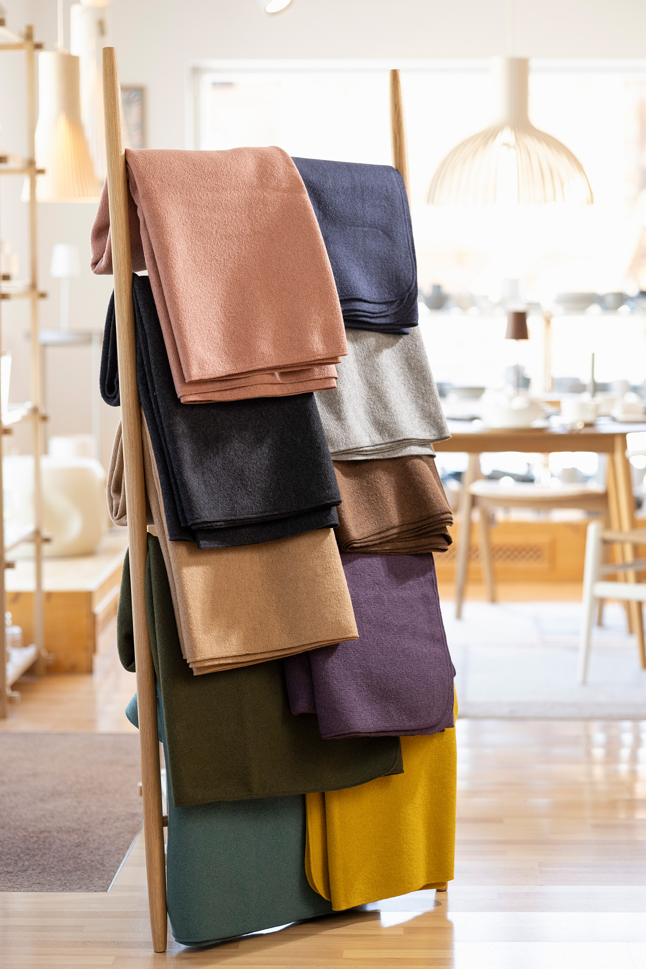 disana Walk-Decken in allen 10 Farben, gefaltet an einer Holzleiter im Verkaufsraum präsentiert, Wollwalk aus Bio-Merinowolle