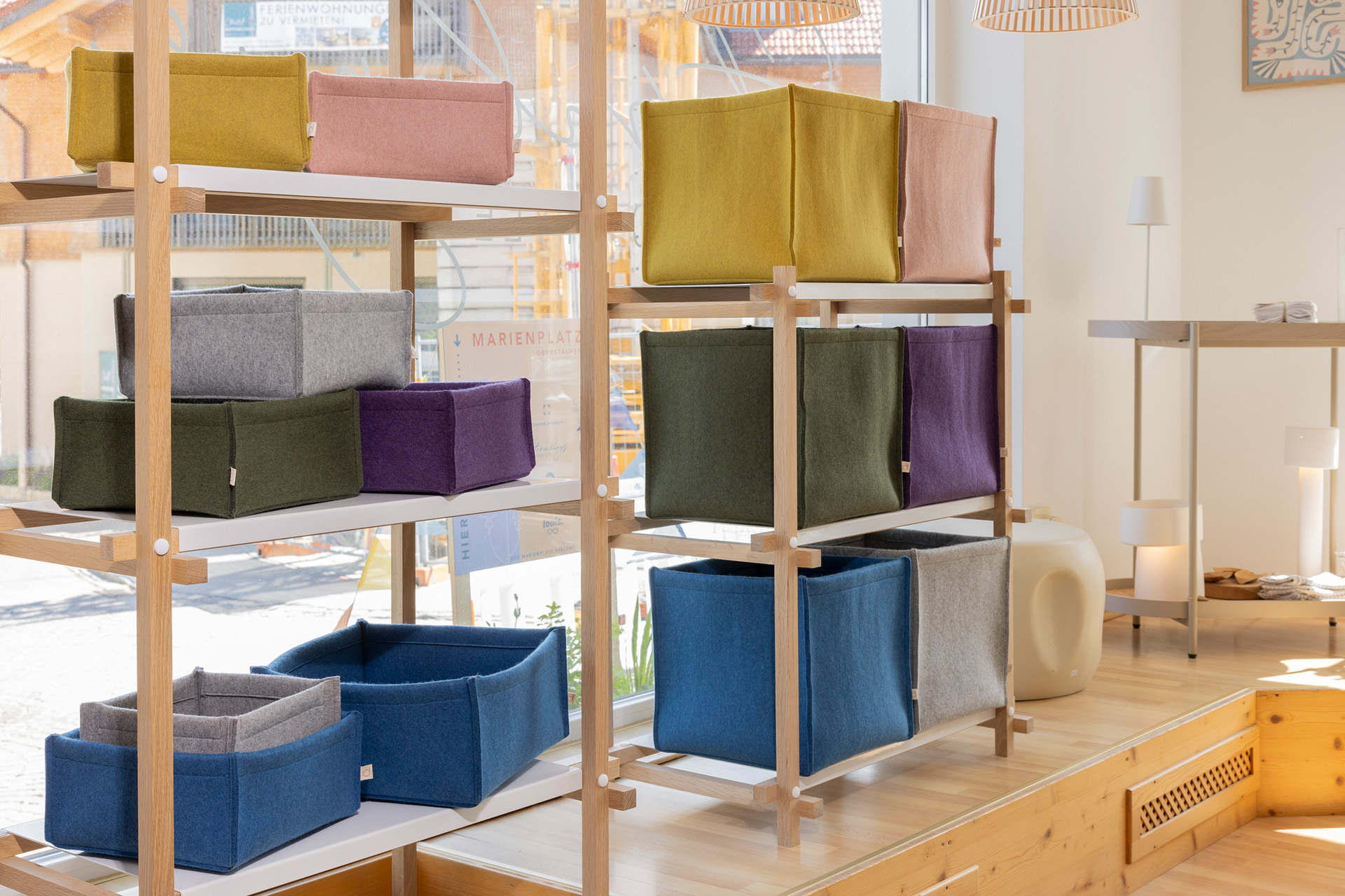 Bunte disana Filz-Boxen in verschiedenen Größen und Farben in einem Holzregal vor einem hellen Ladenfenster
