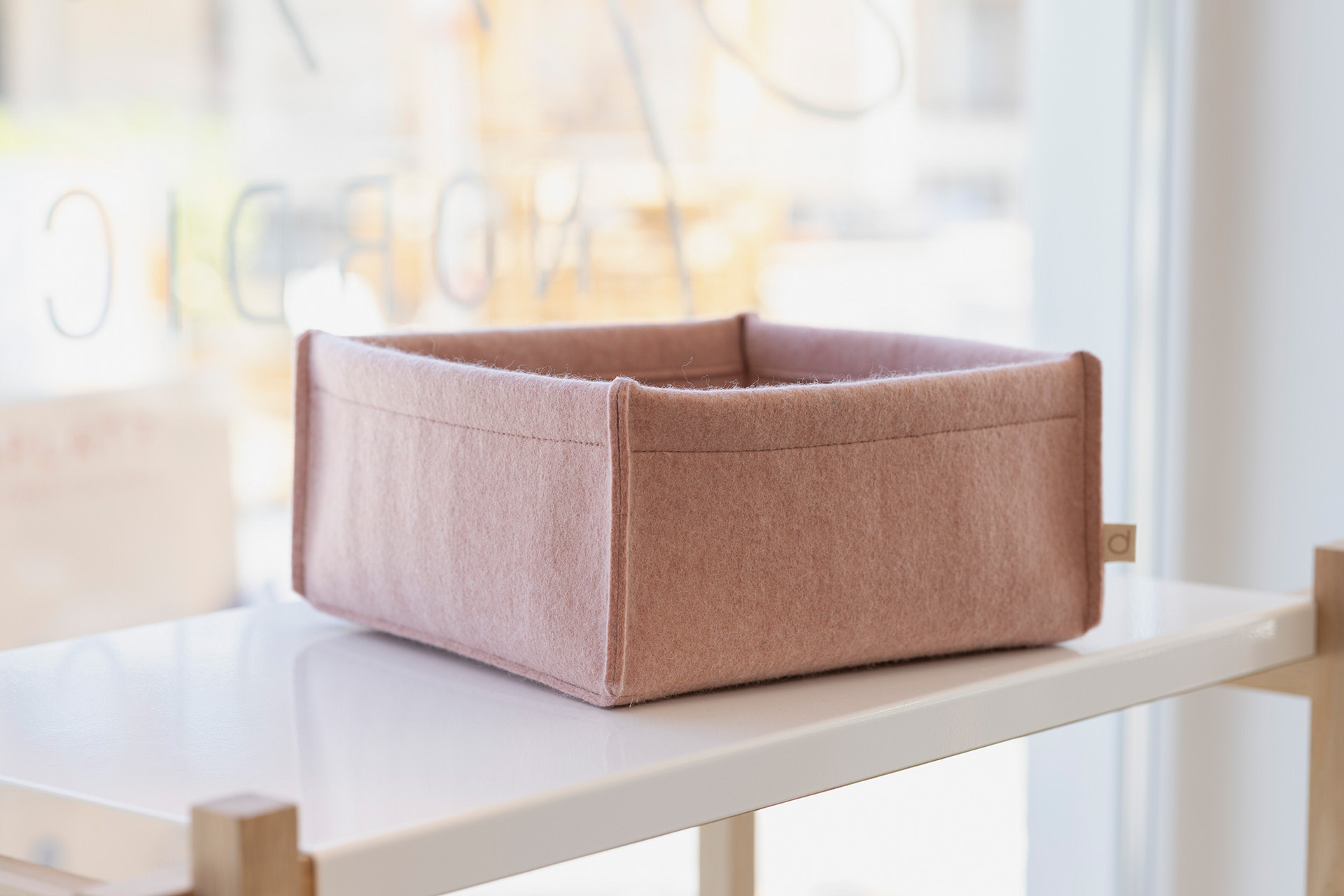 Kleine roséfarbene disana Filz-Box aus Bio-Recycling-Filz auf einem weißen Regal vor einem hellen Fensterhintergrund.