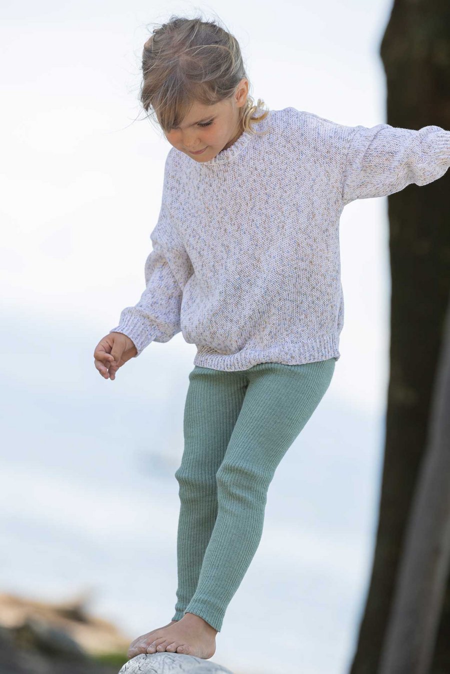 Mädchen im disana Baumwoll-Pullover "Spray", Spray Natur & Strick-Leggings, Jade  balanciert draußen und schaut nach unten