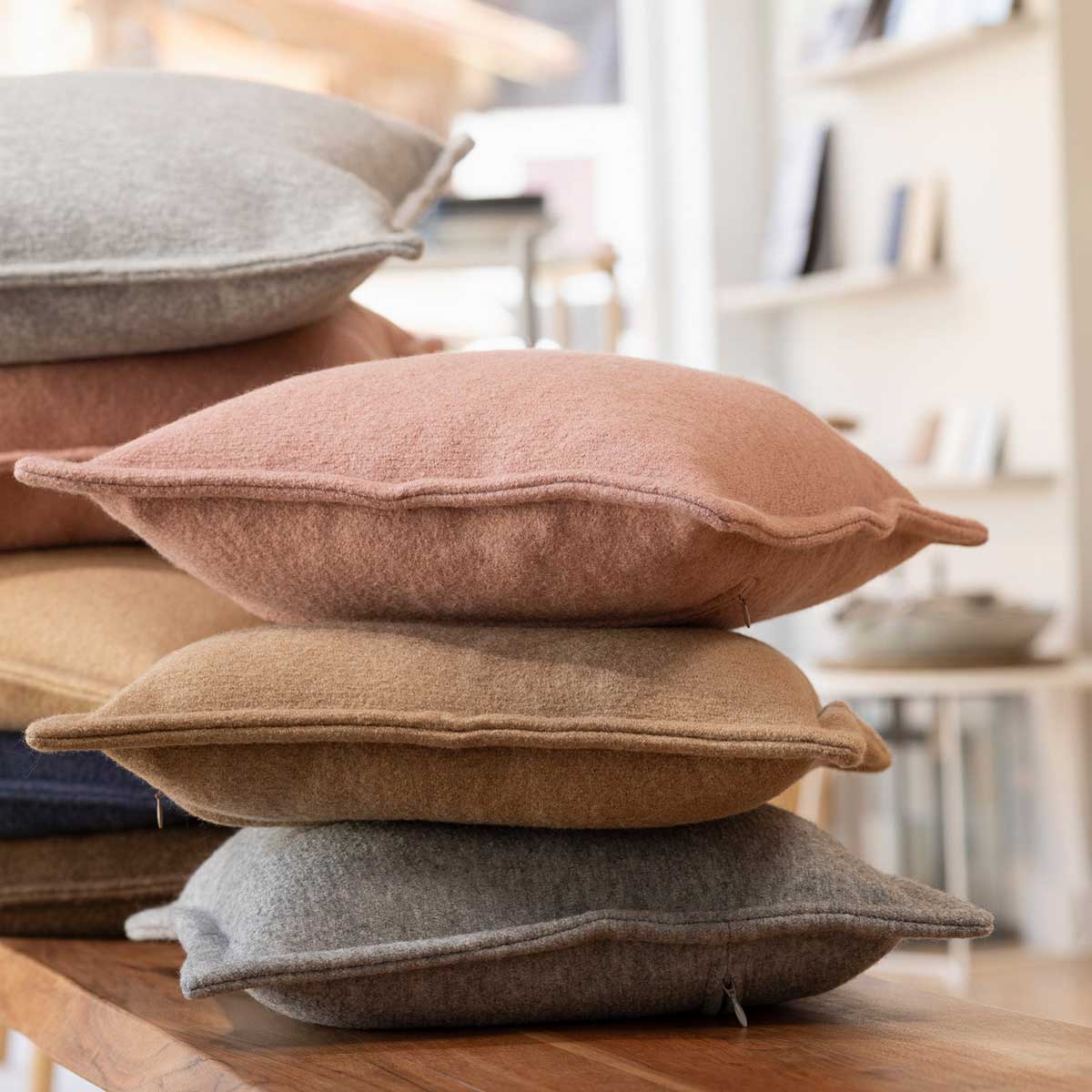 Gestapelte Kissen mit disana Walk-Kissenhüllen in Rosé, Karamell & Grau in einem hellen Raum - weitere Kissen im Hintergrund