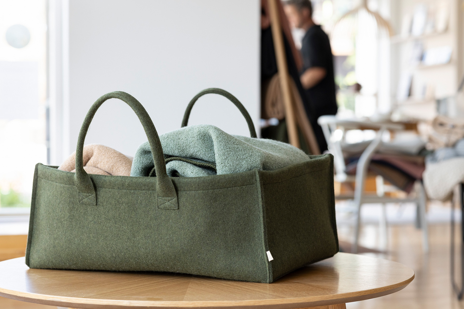 Großer disana Filz Aufbewahrungs-Korb in Oliv mit Tragegriffen, gefüllt mit Decken aus Bio-Merinowolle auf einem Holztisch