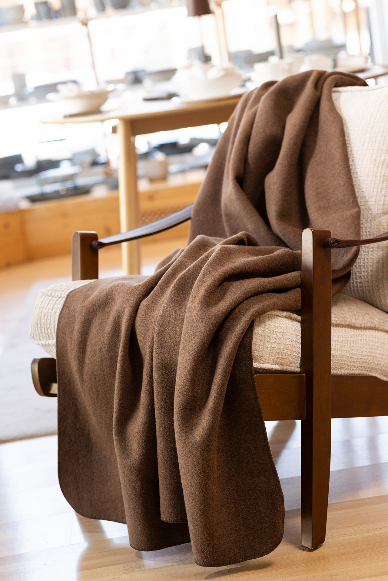 disana Walk-Decke in Haselnuss über einem Holzsessel mit beigem Bezug drapiert in einem hellen Raum, Wollwalk Bio-Merinowolle